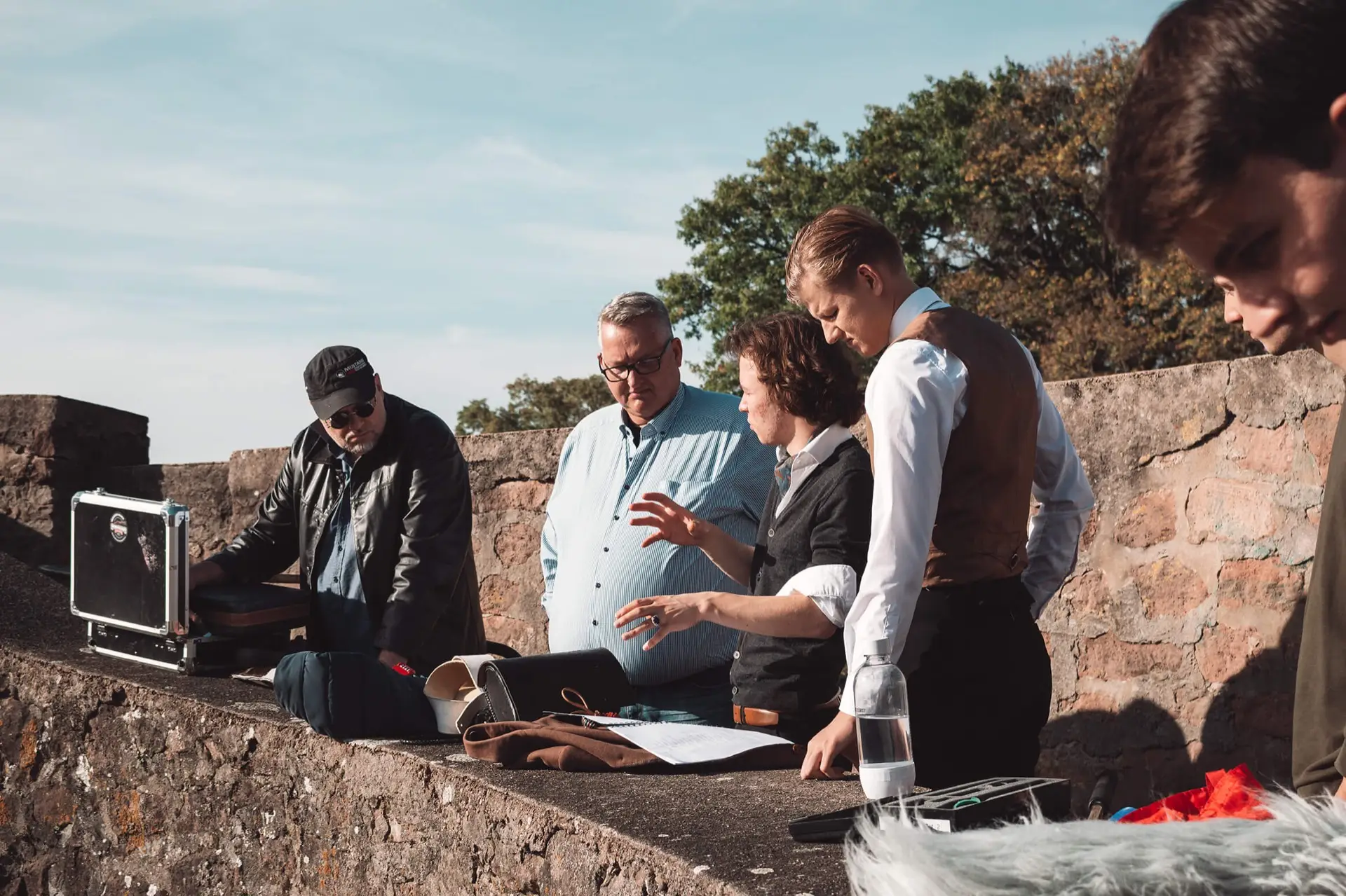 Outdoor film shoot: the crew discusses the next shot by a stone wall